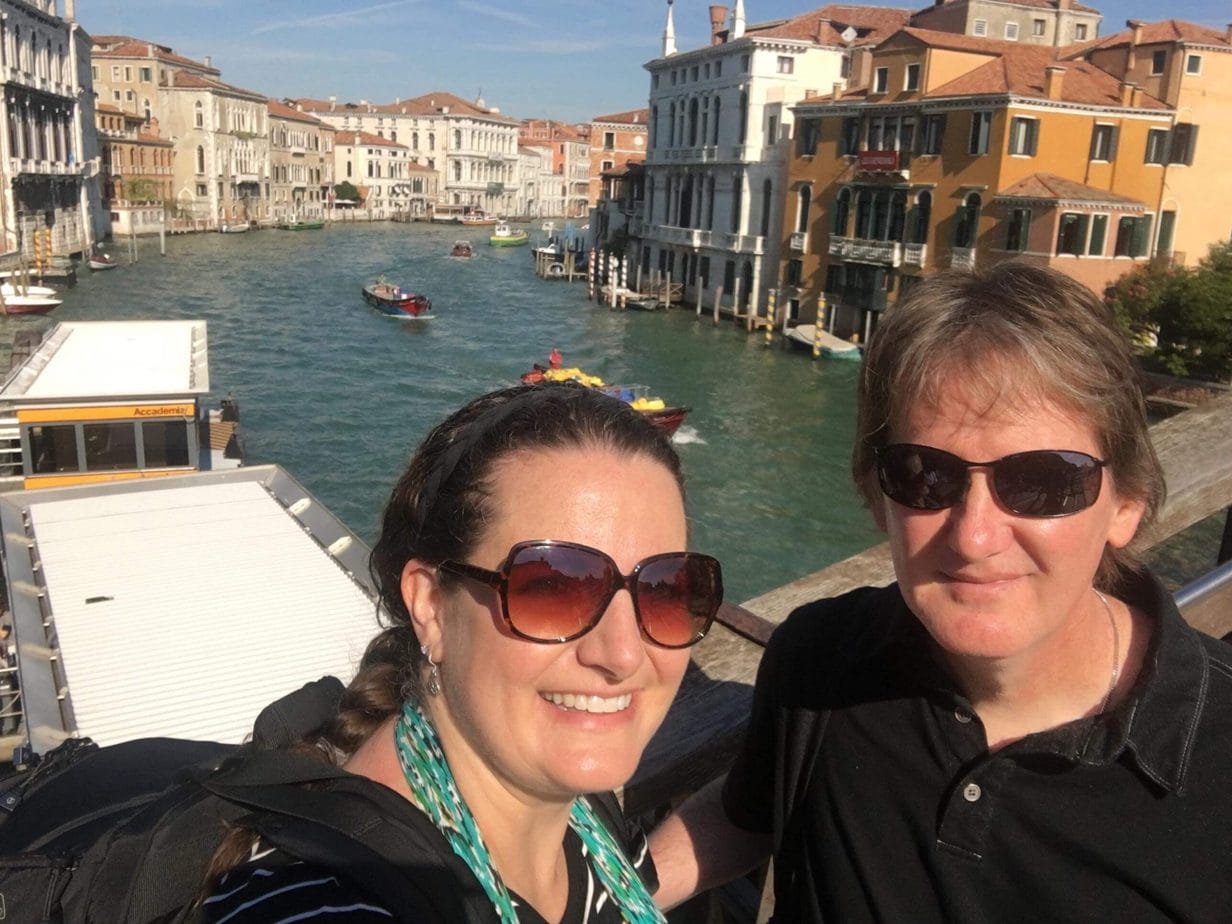 www.redneckrhapsody.com Tuesday Travel - Wendy and Jay Gregory on a bridge in Italy with water, boats, and city behind them.