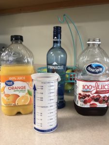 Ingredients for a fruity vodka Cocktail -Orange juice, whipped vodka, cranberry juice, and a measuring cup