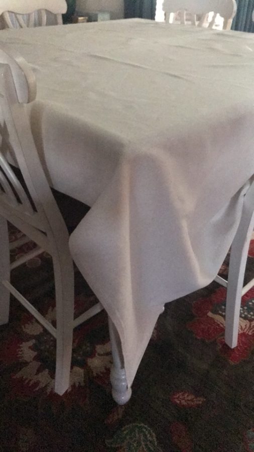 Arrange the tablecloth on table to determine amount of overhang needing to be removed. 